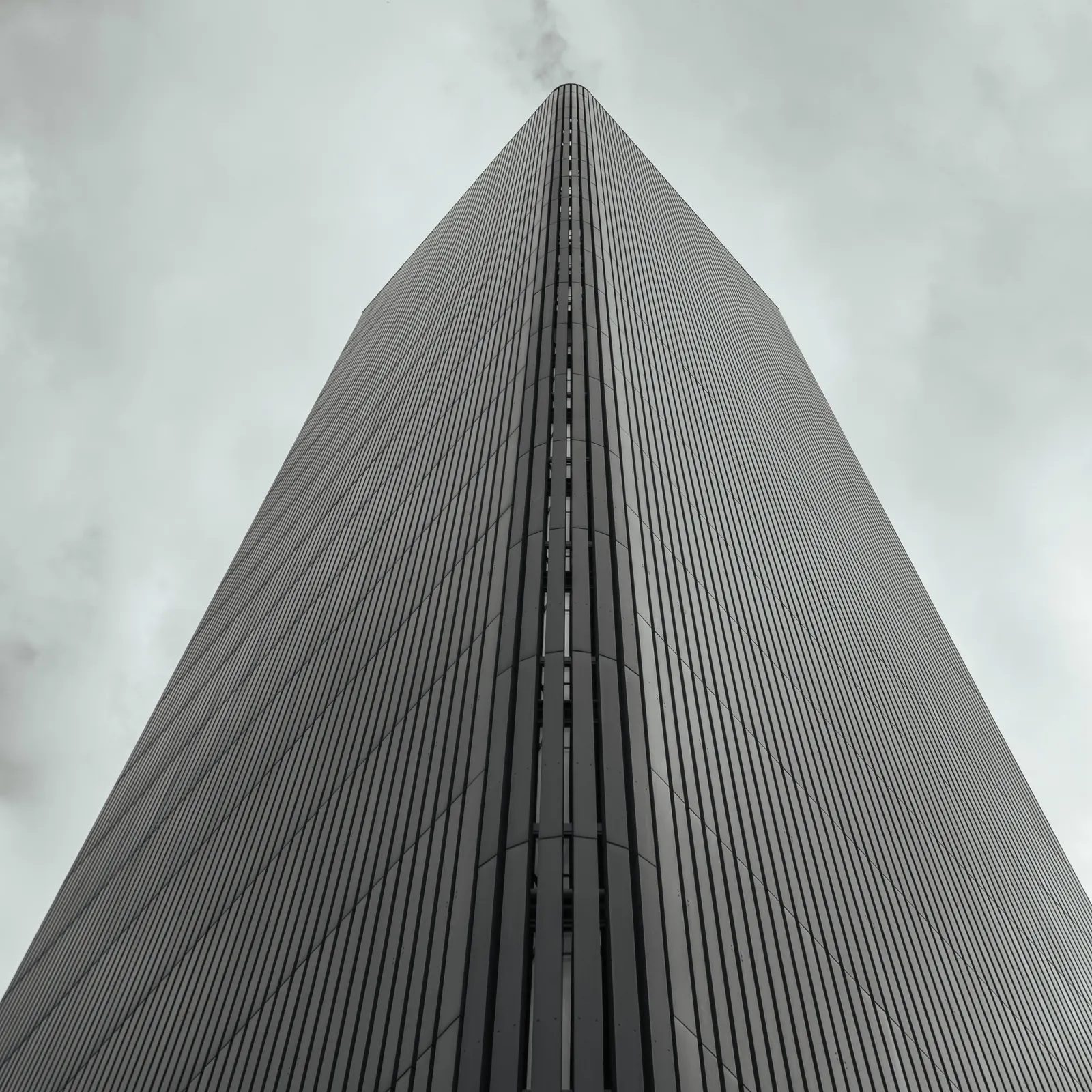 A tower photographed from below, its corner dividing the frame against an overcast sky